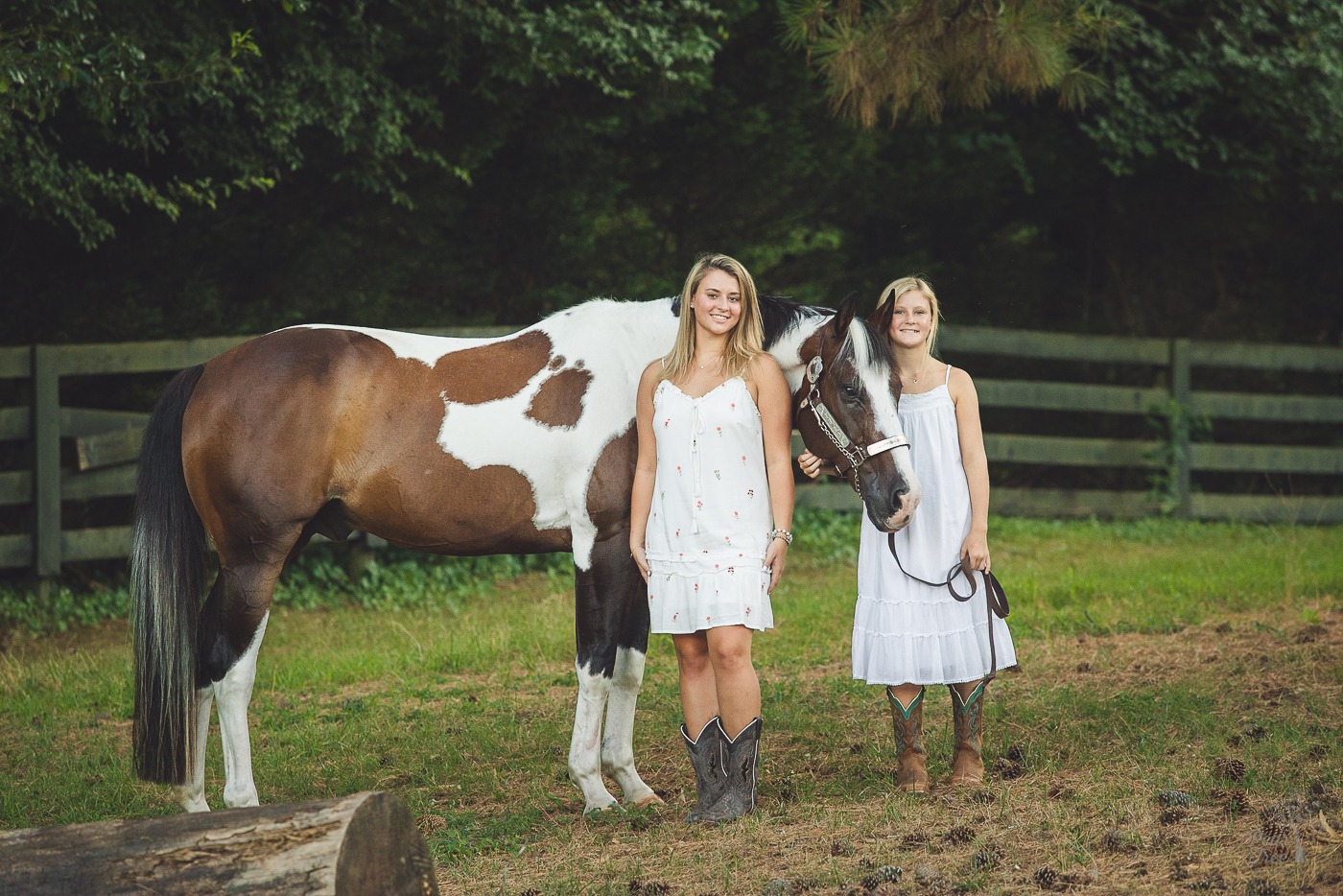 Two smiling sisters in white sundresses smiling with their paint horse in Woodstock during a high school senior session