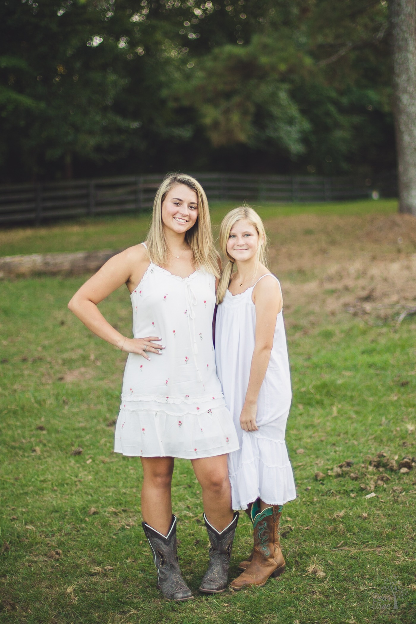 Two blonde and smiling teenage sisters in white sundresses and cowgirl boots