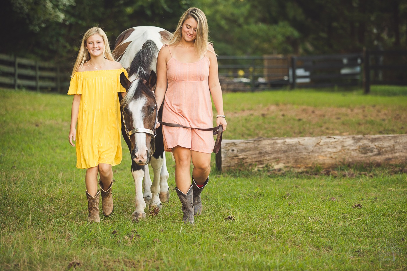 Two sisters in sundresses and cowgirl boots walking their paint horse through a field during their photoshoot in Woodstock, GA