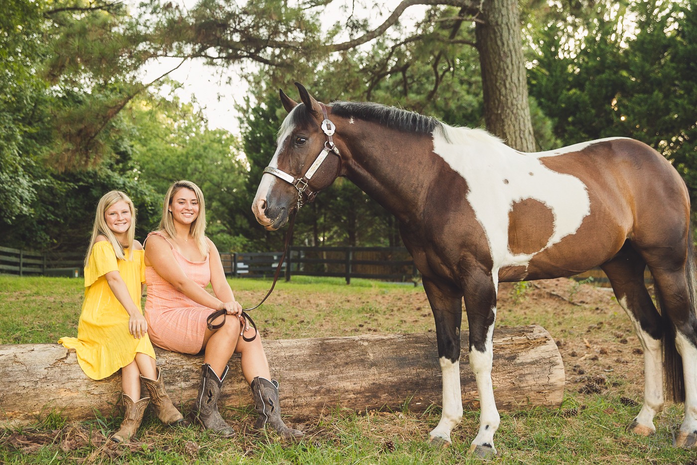 Two sisters in sundresses and cowgirl boots sitting on a log next to their paint horse in Woodstock, GA