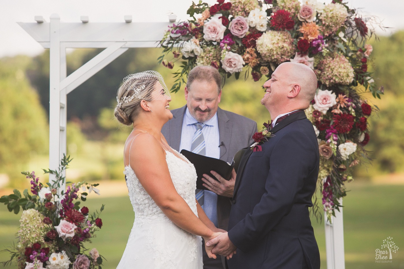 Bride and groom laughing at Cumming Polo Fields wedding arbor with flowers behind them