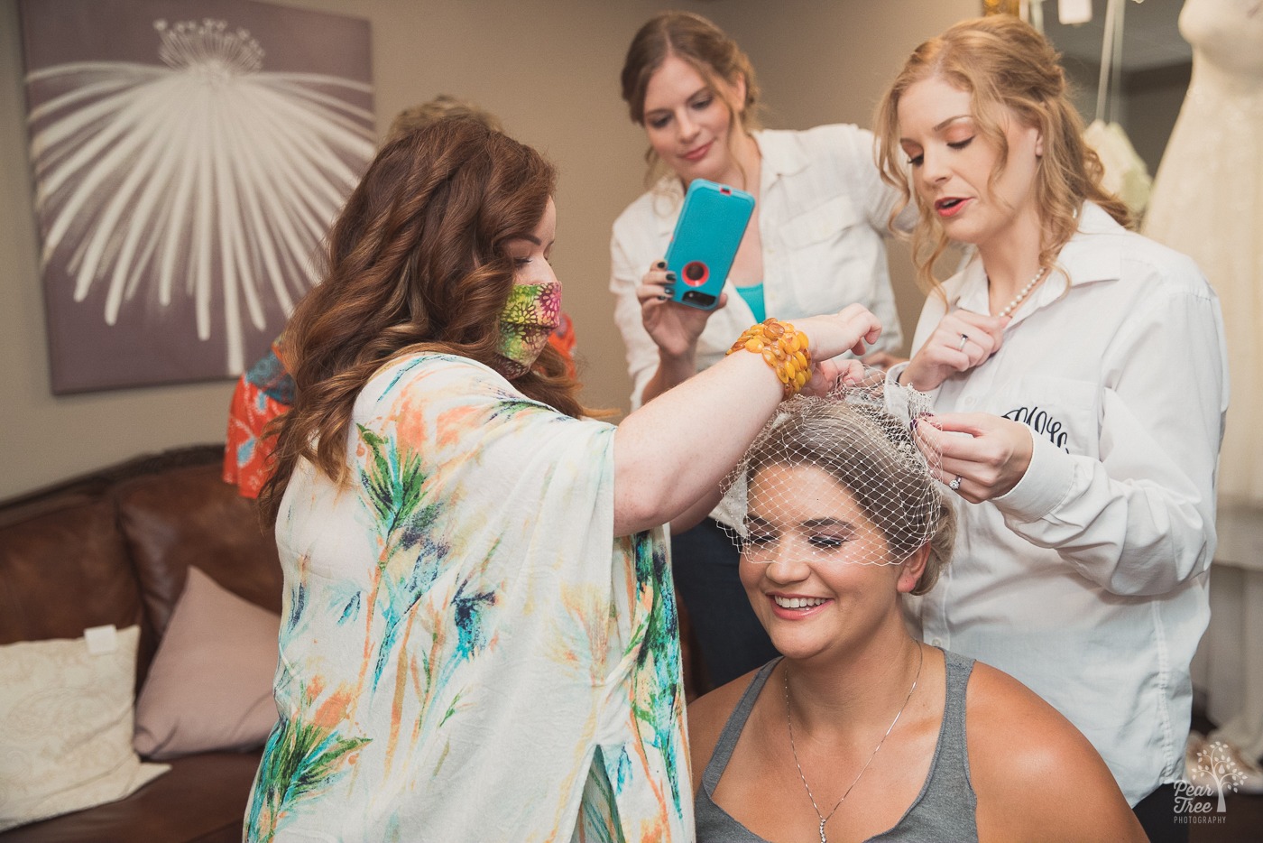 Sisters and hair stylist helping attach veil to bride's head
