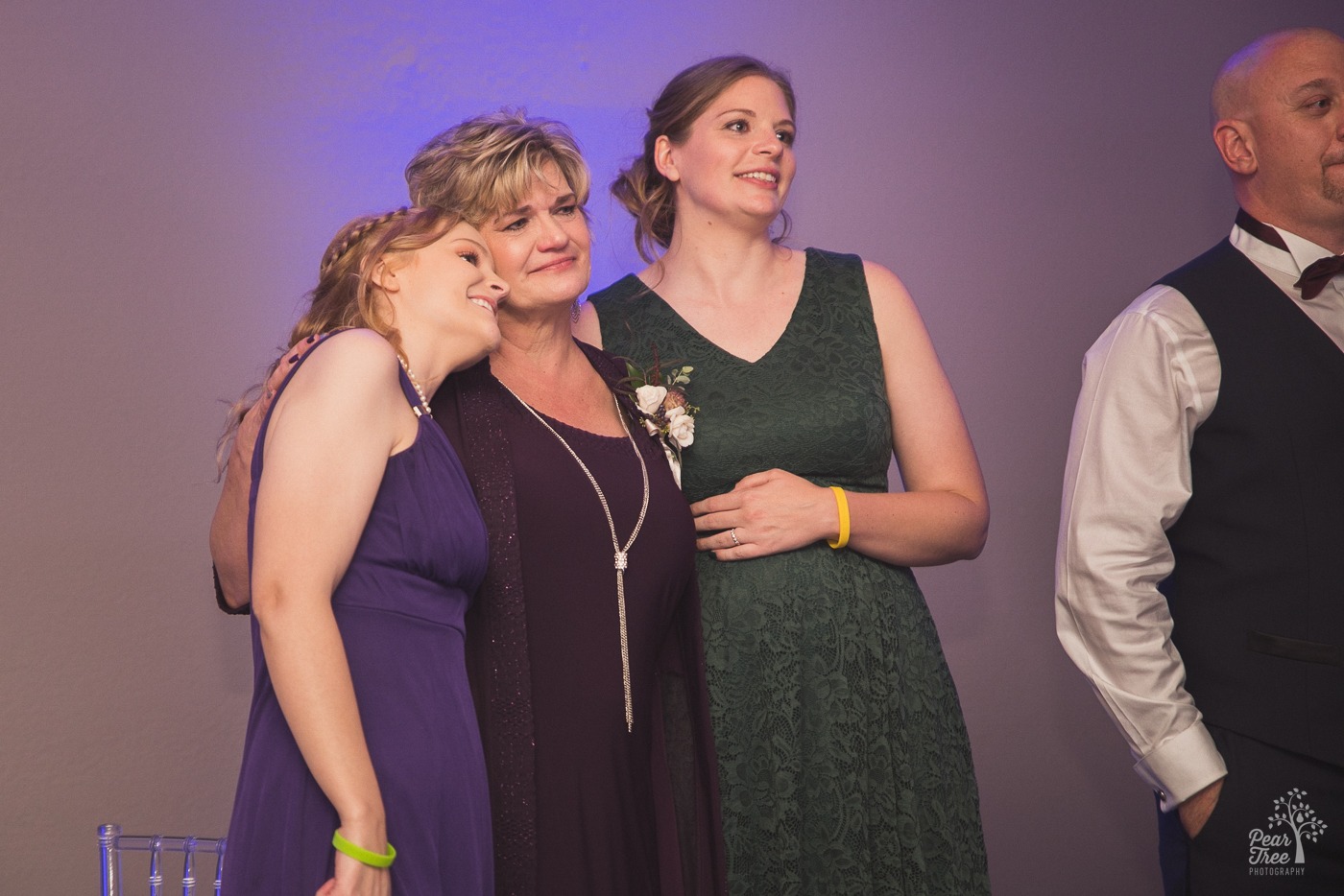 Bride's mom and two sisters hugging and crying while watching bride dance with dad