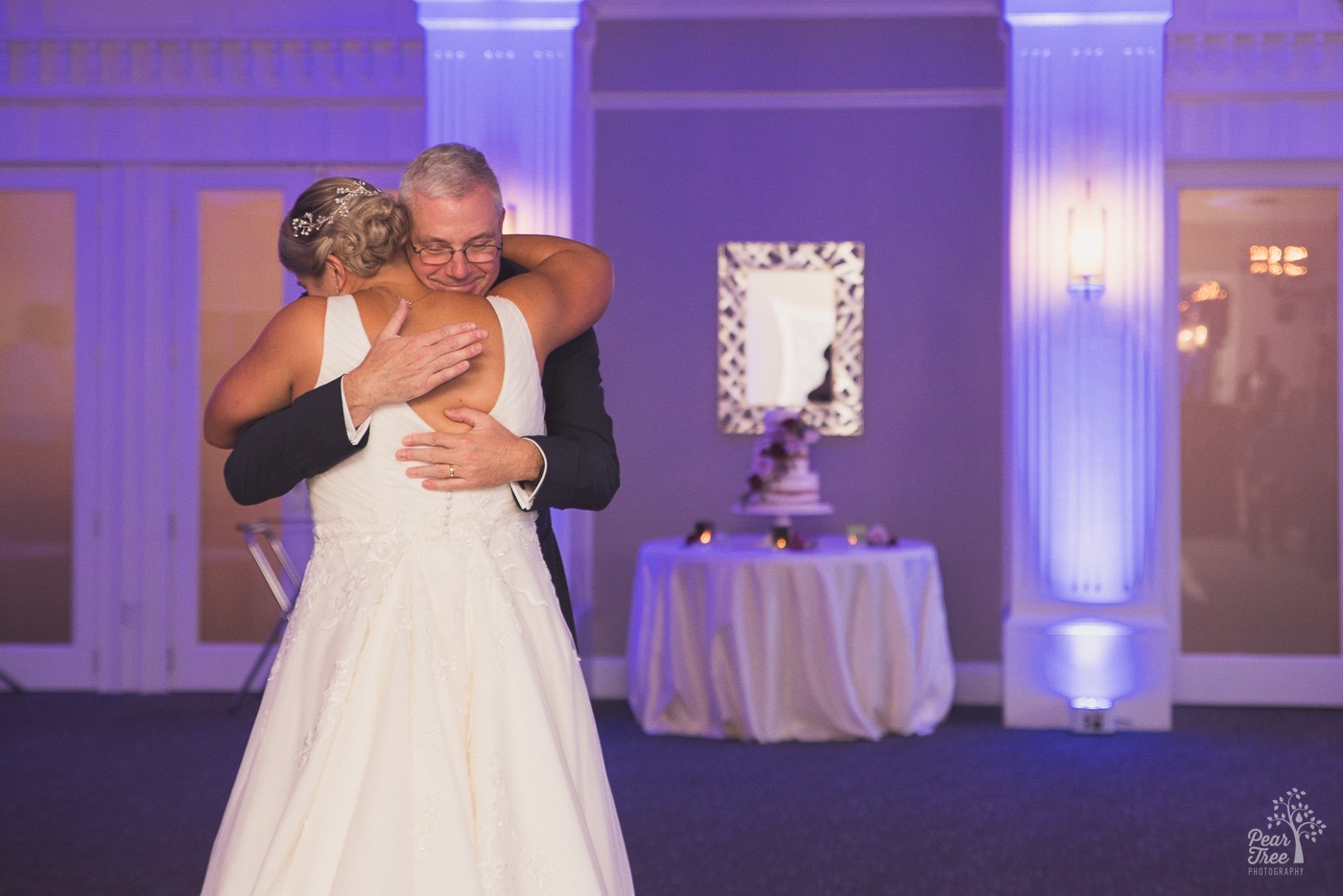 Bride hugging her dad with wedding cake in the background