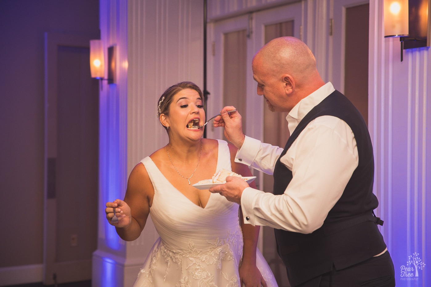 Bride opening her mouth for cake from the groom with a funny expression