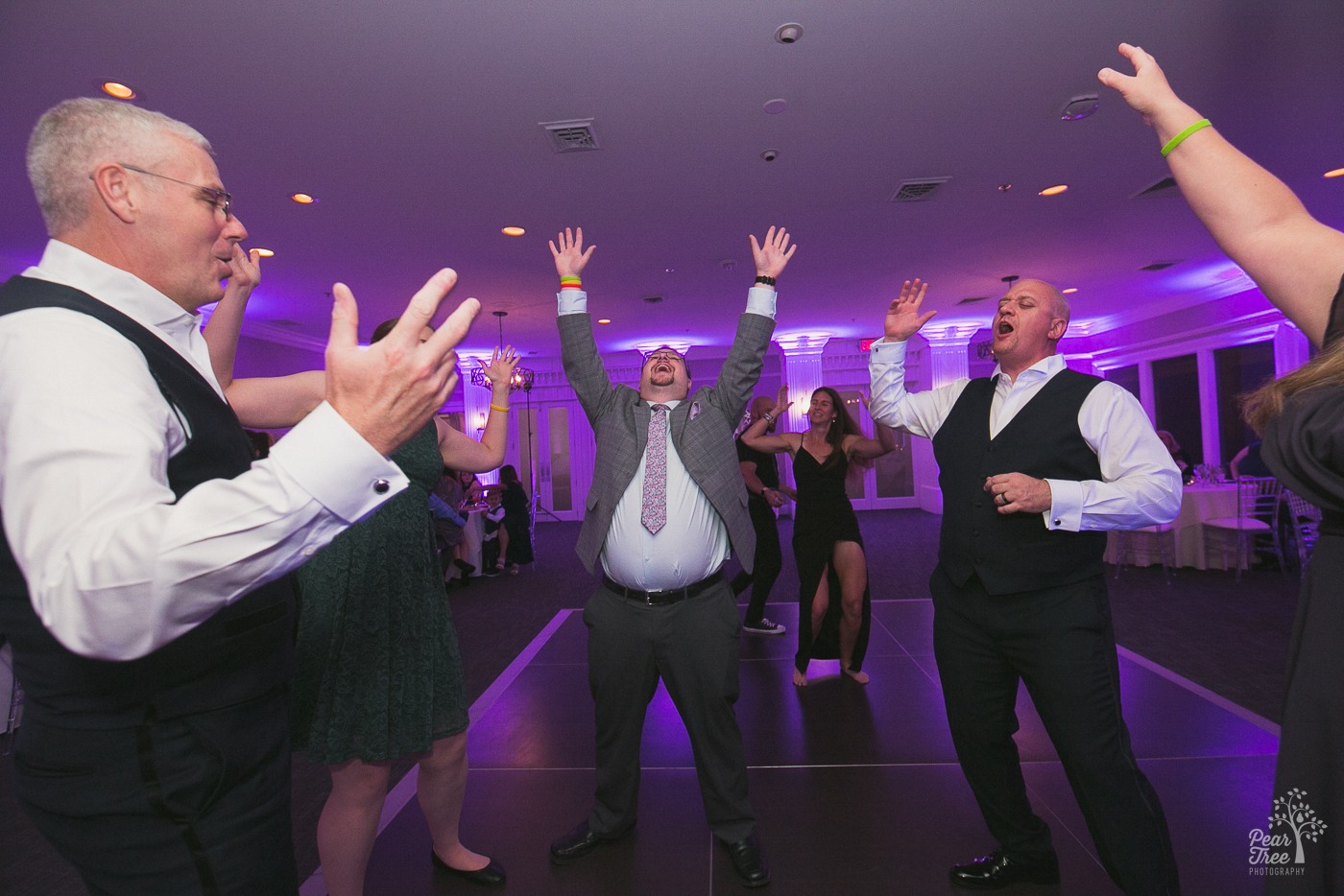 Groom with friends and family singing and raising hands on the dance floor