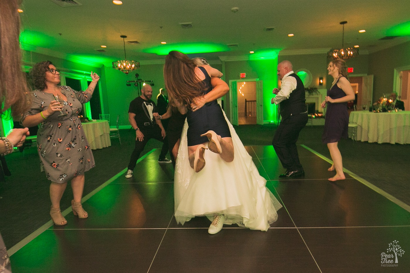 Woman lifted off the dance floor with her feet in the air as the bride spins her