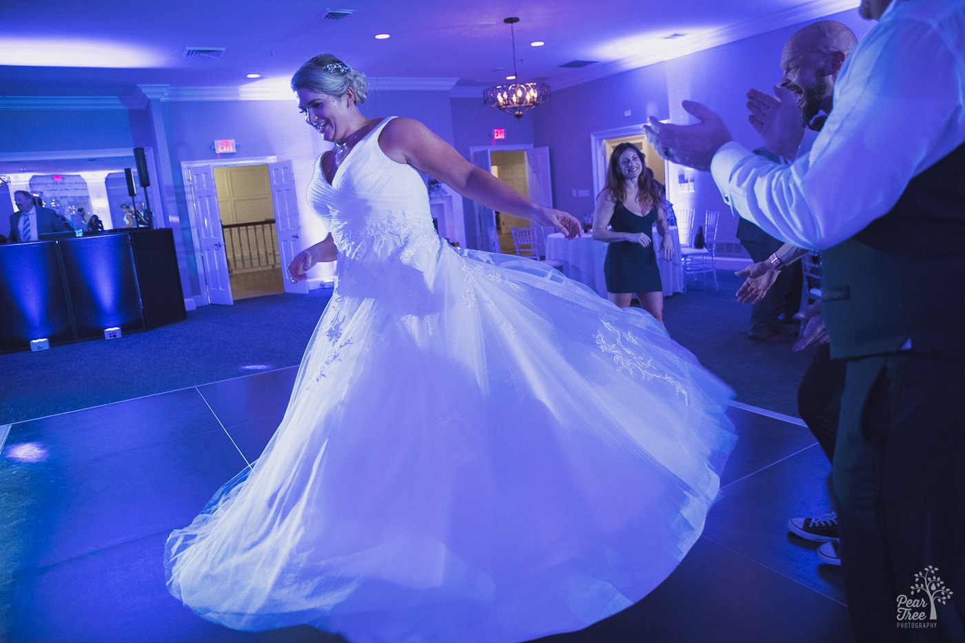 Beautiful blond bride spinning on the dance floor as her wedding dress flares out under purple lights