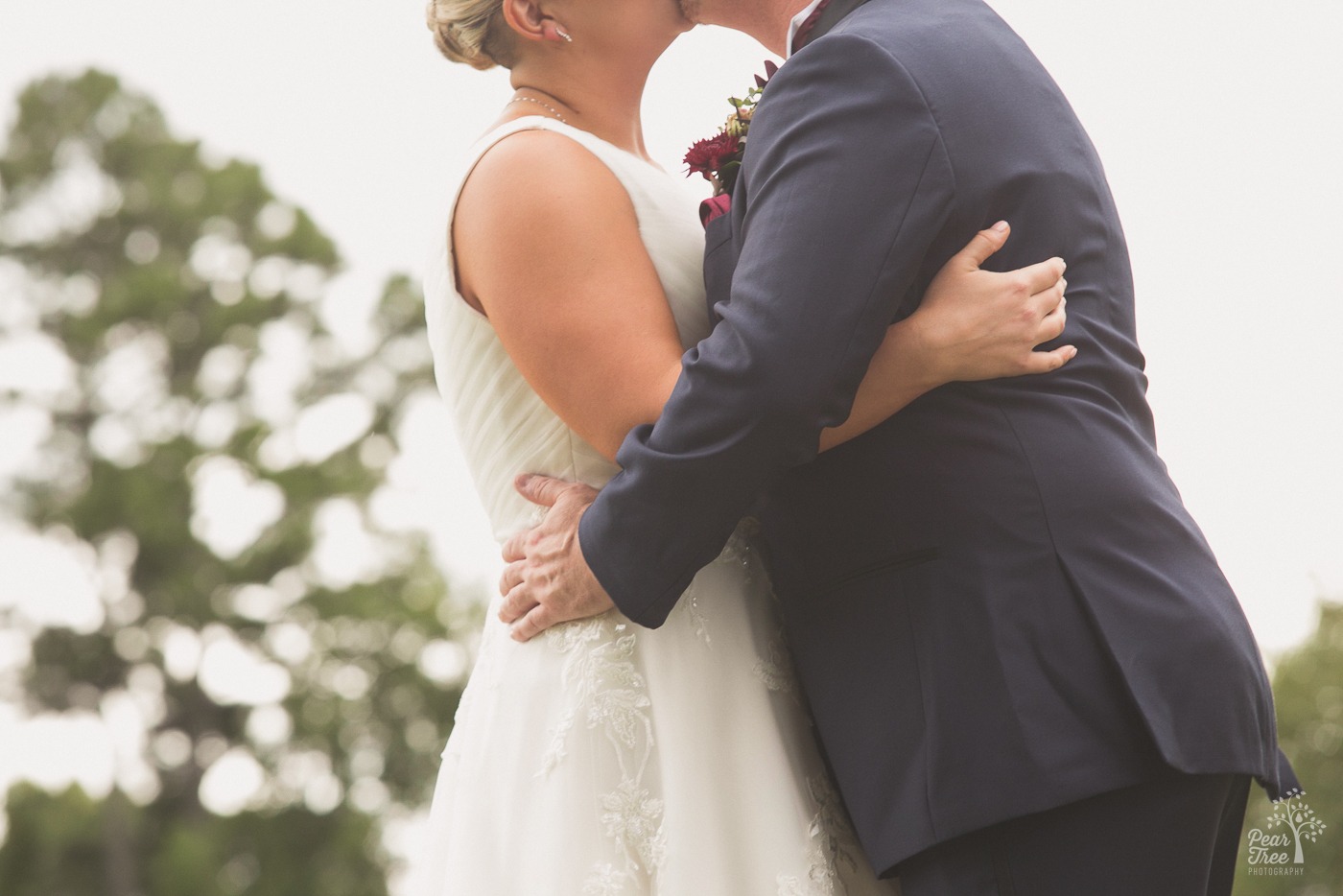 Anonymous bride and groom kissing with hands stretching around each other's waists