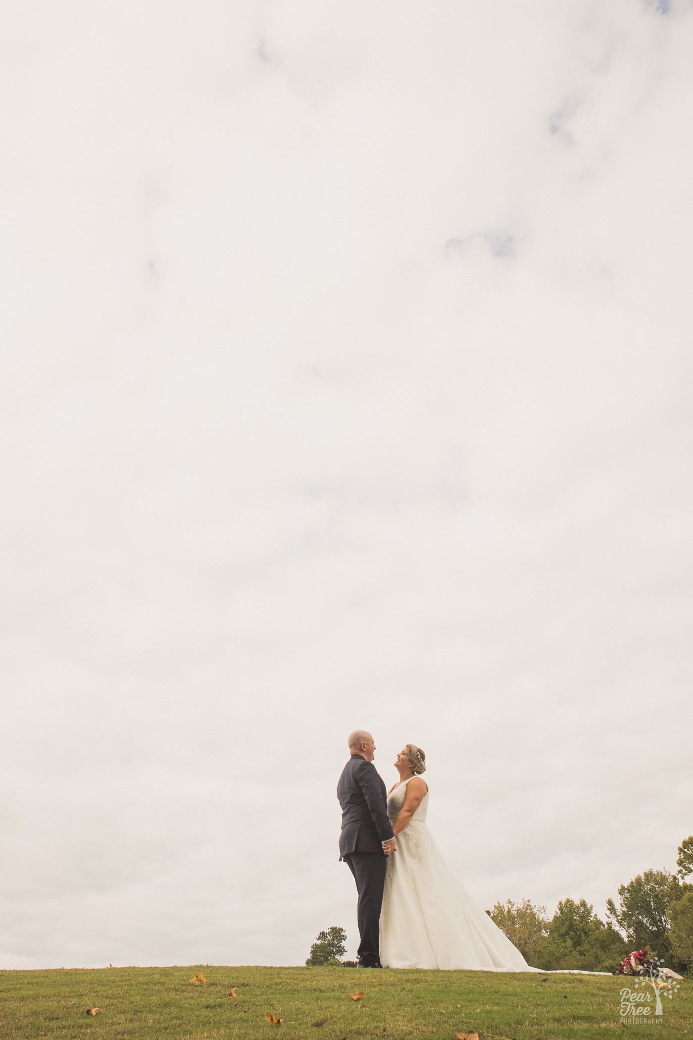 Bride and groom standing close on a hill with big sky over them