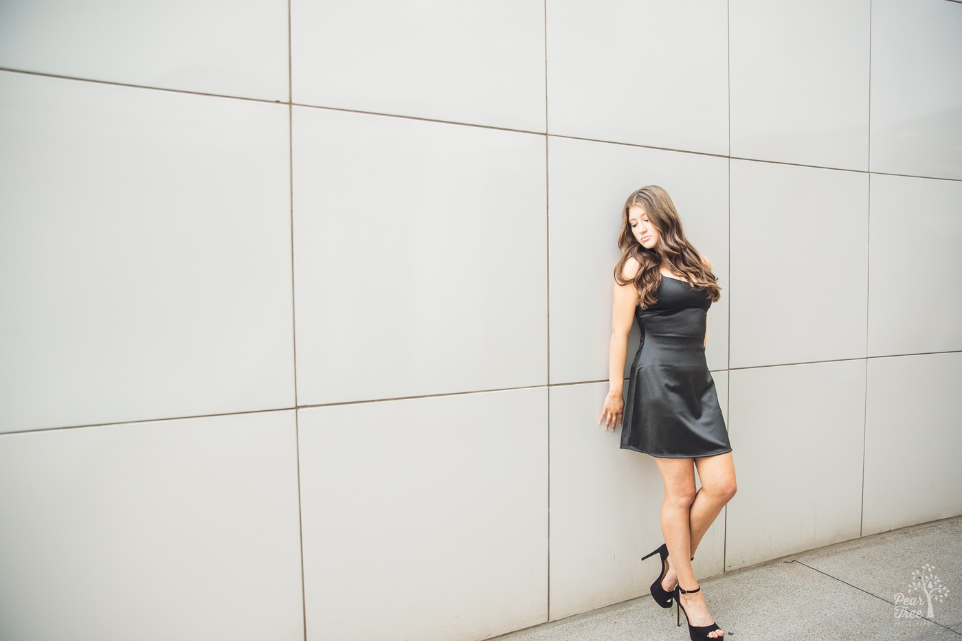 Gorgeous high school senior girl in black silk dress, high heels, and long wavy hair looking away from the camera