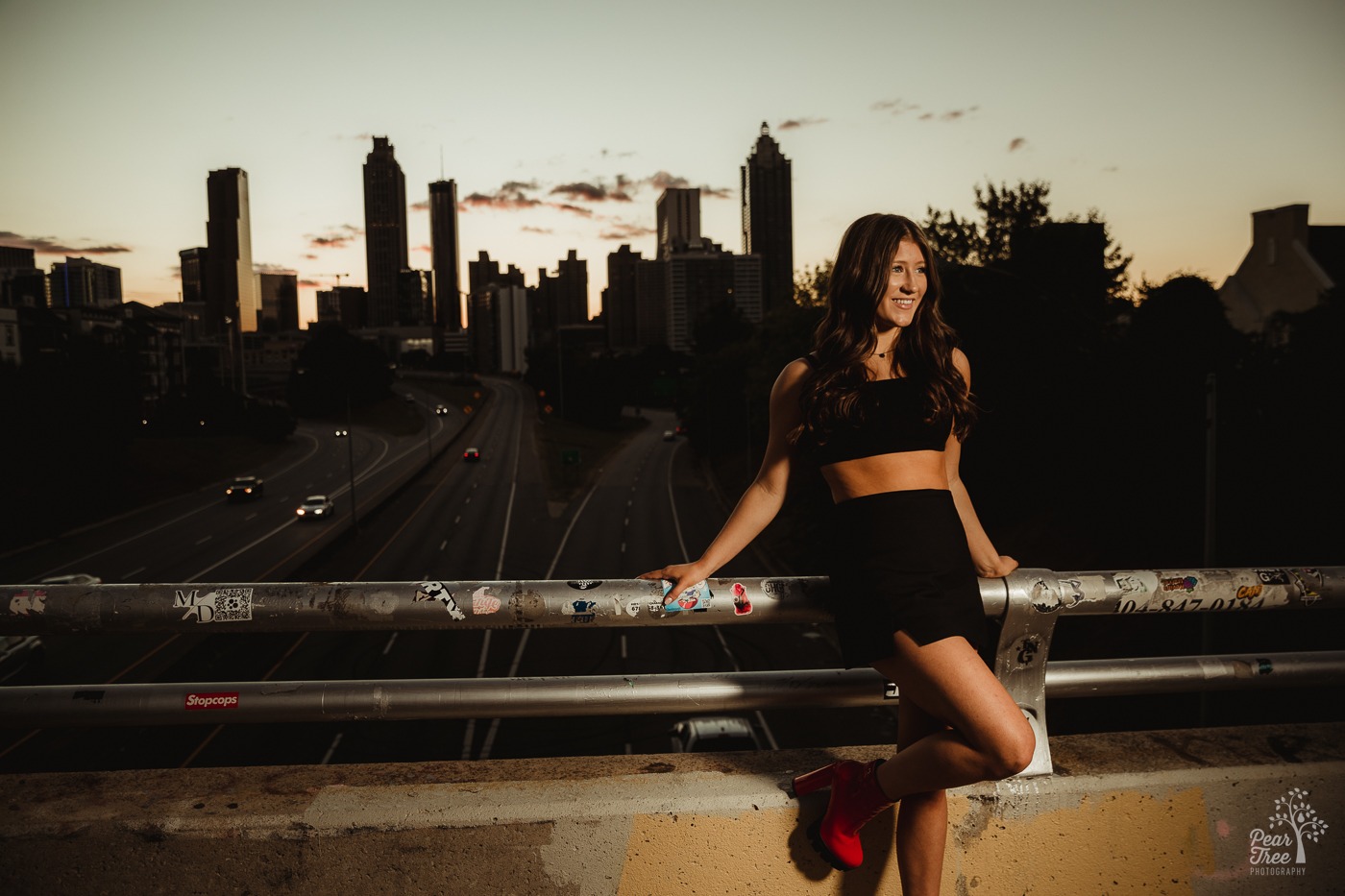 Atlanta high school senior girl on Jackson Street Bridge at sunset with out-of-focus Atlanta skyline behind her