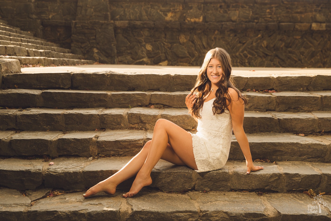 Barefoot high school senior girl sitting on Piedmont Park steps smiling and playing with her hair