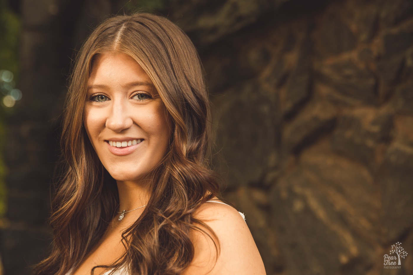 Beautiful teenage girl with brown wavy hair and striking green eyes is smiling while looking at the camera