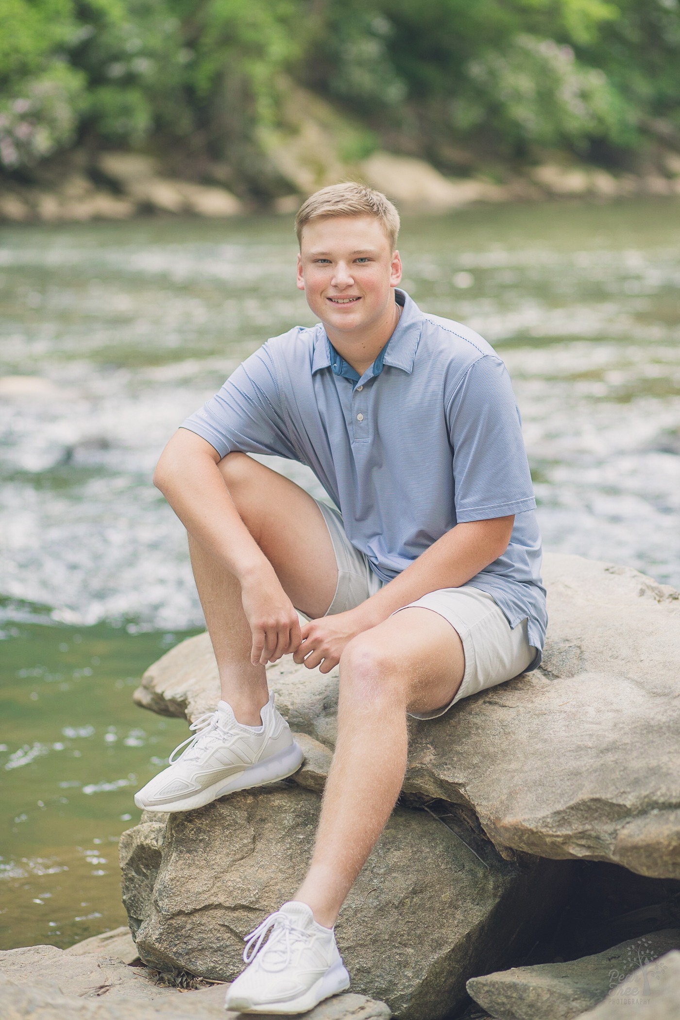 Woodstock High School senior boy sitting on rocks and smiling in front of Vickery Creek at Roswell Mill