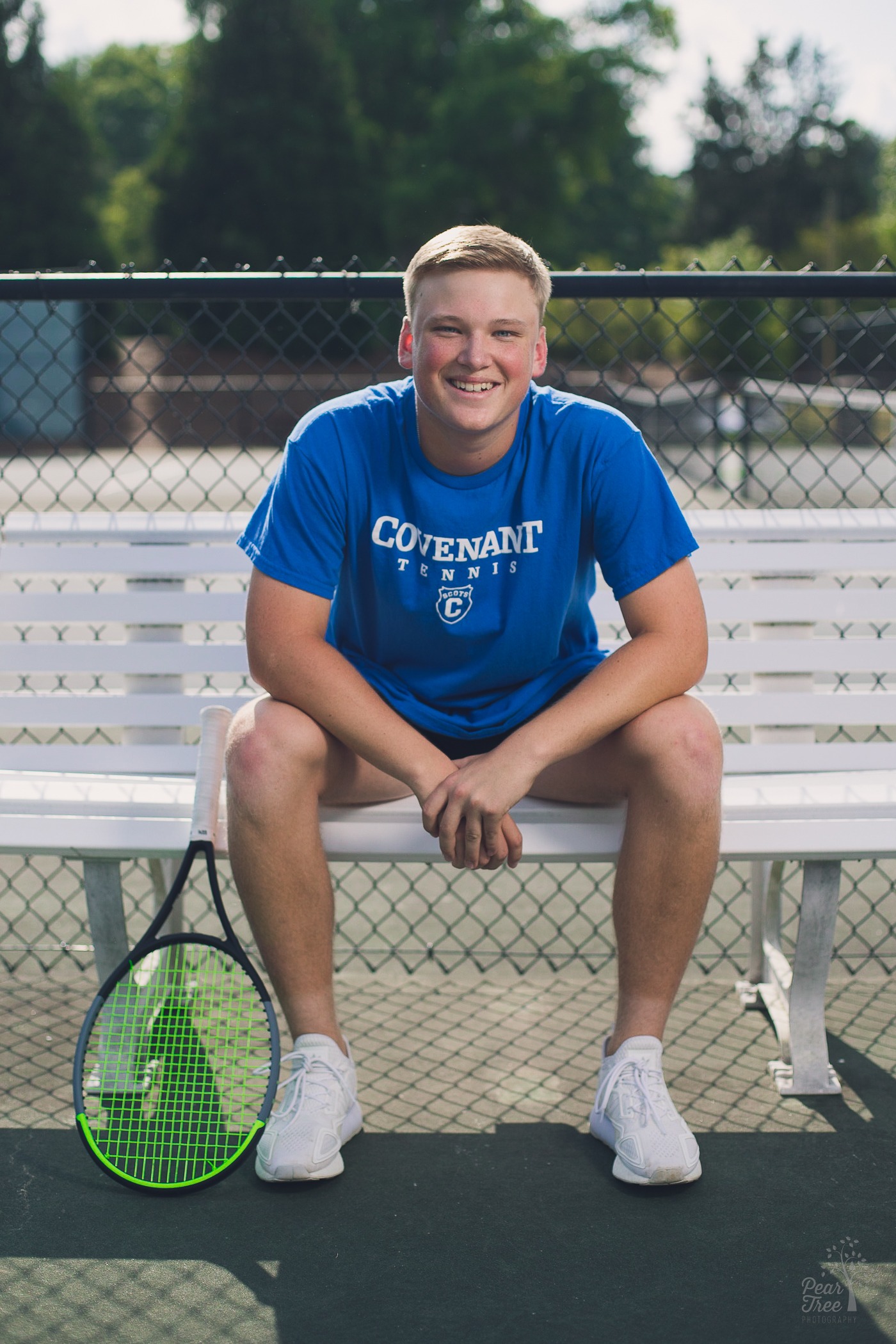 Woodstock High School Senior boy sitting on tennis bench smiling with his racquet next to him