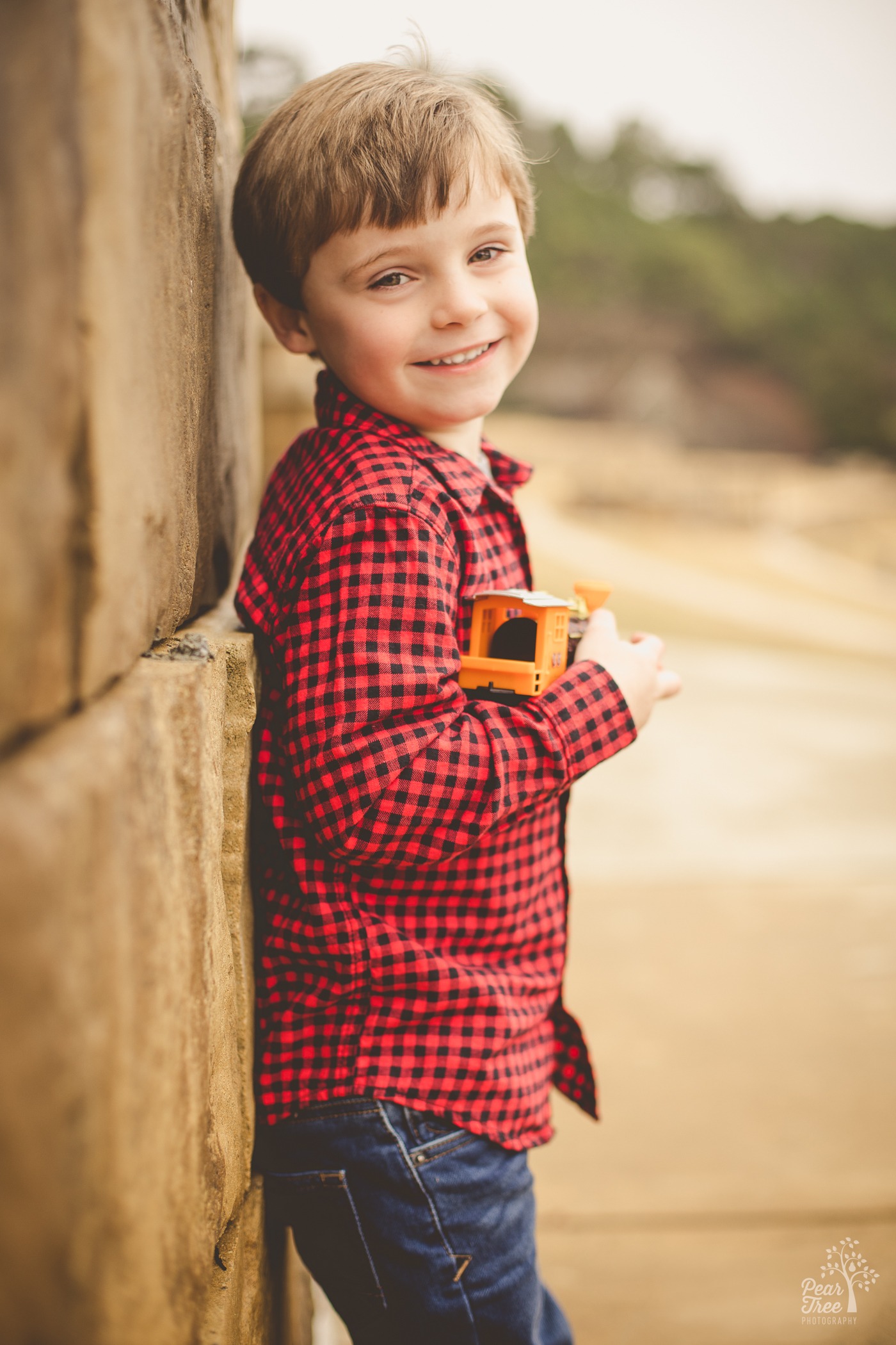 Four year old photoshoot in downtown Woodstock with the cutest little boy in a red checked shirt holding his toy train and smiling