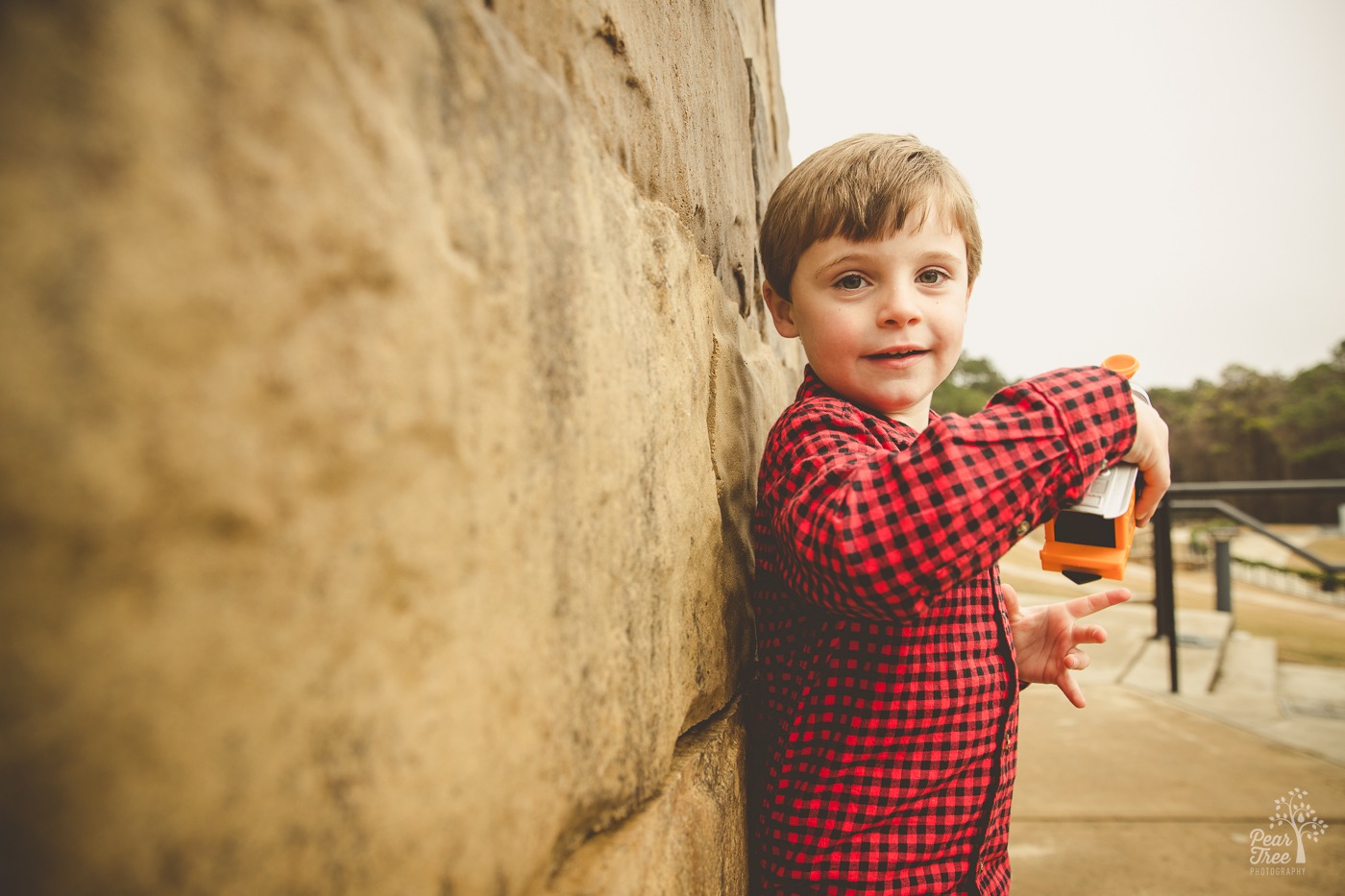 Little boy in a red checked shirt smiling just a little as he plays with his train