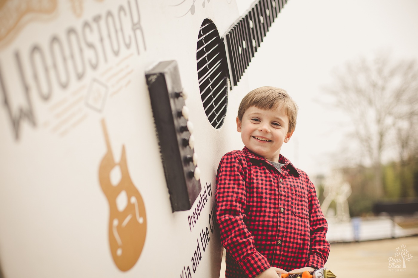 Four year old photoshoot with a boy smiling big and standing proudly against the Woodstock guitar