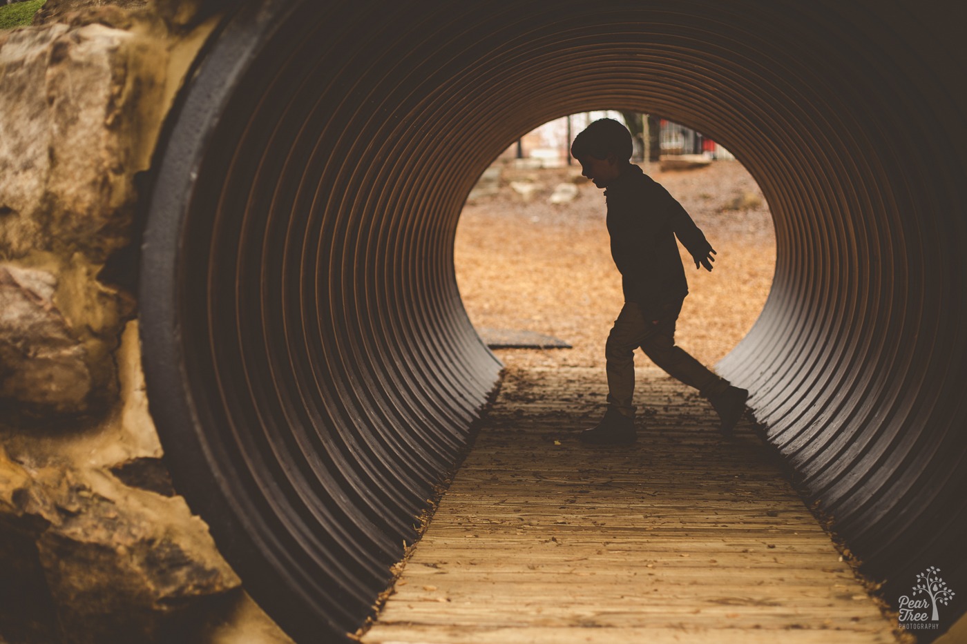 Silhouette of a four year old boy running through a tunnel in a downtown Woodstock playground