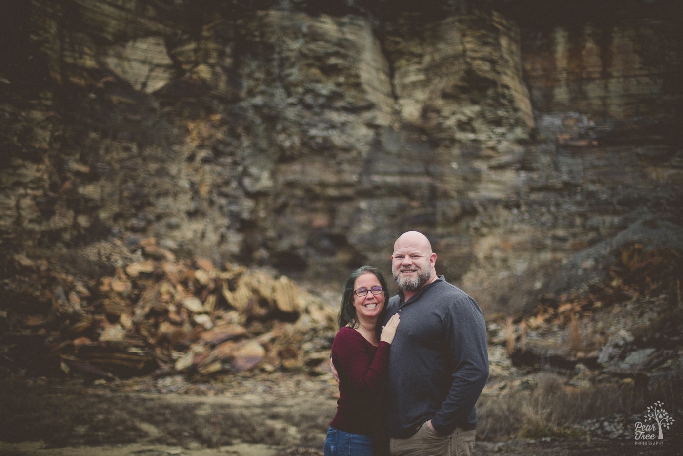 Smiling couple standing close and looking at the camera in front of a big rock wall