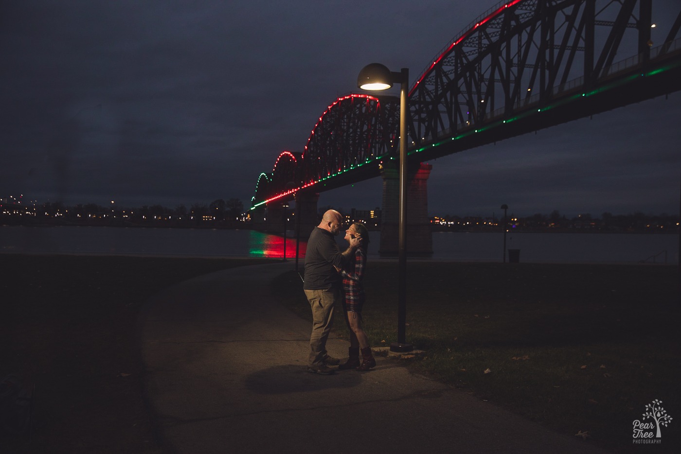 Night time photograph of a couple facing each other and touching under the Big Four Bridge in Louisville