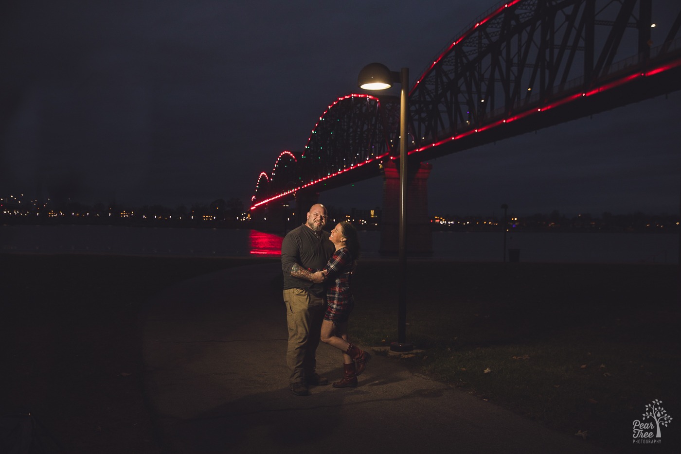 Night time photograph at Big Four Bridge in downtown Louisville with a smiling couple holding each other