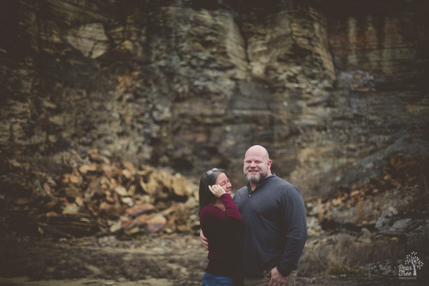 Laughing woman brushing her hair out of her face while her bearded boyfriend smiles at the camera