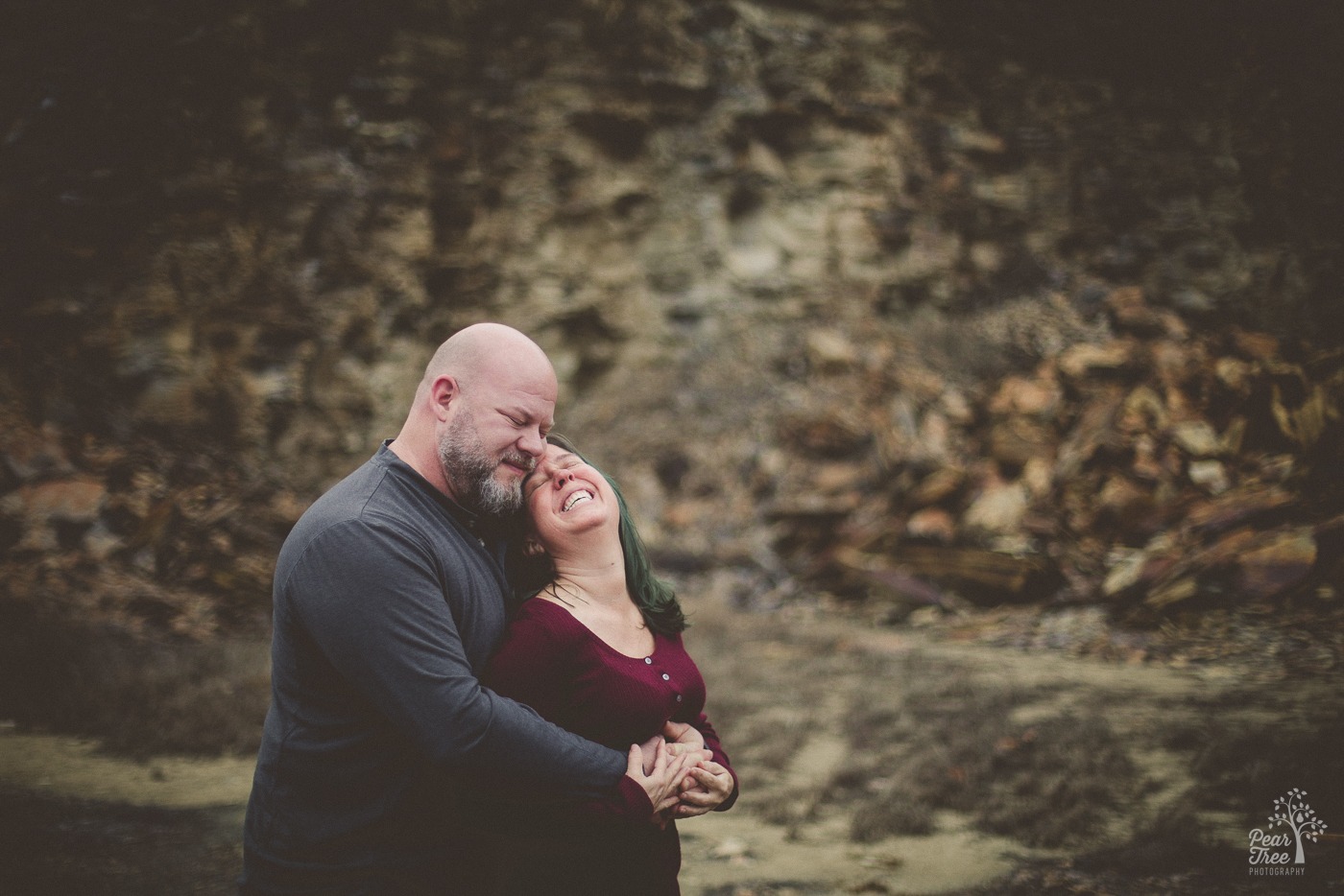 A bearded man smiling with his eyes closed while he holds his laughing girlfriend close