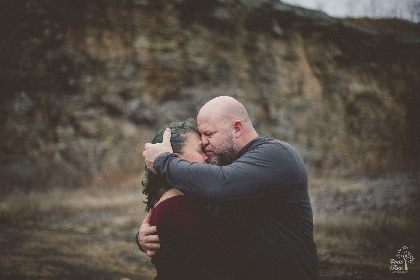 A bearded man holding his girlfriend close with his hands wrapped around her back and head