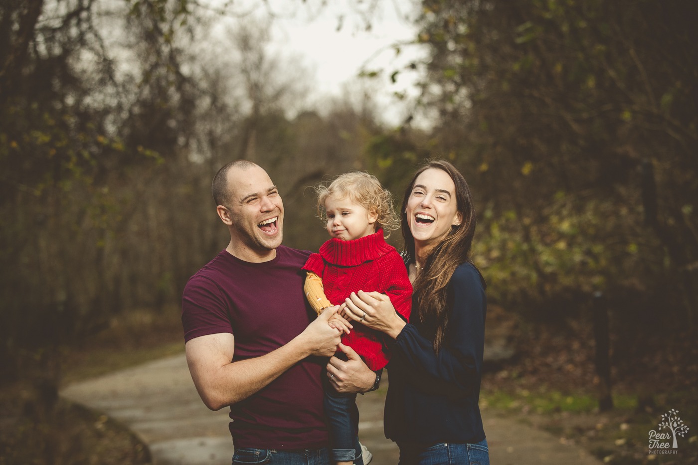 Two cute parents belly laughing with mouths wide open while holding their little girl at Rope Mill Park