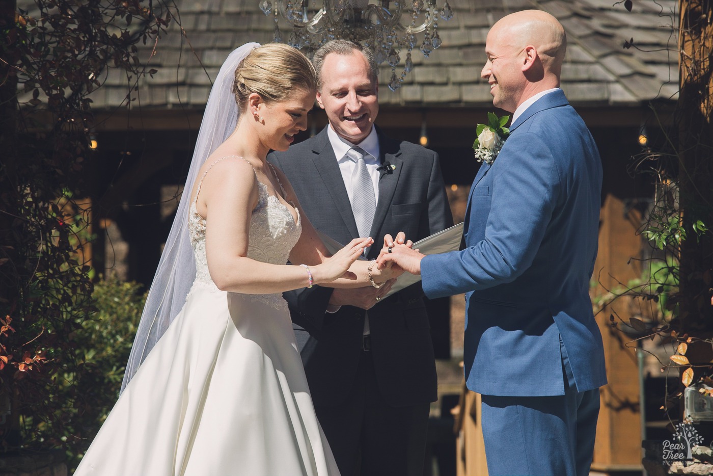 Bride with a long veil sliding a wedding band on her groom's finger