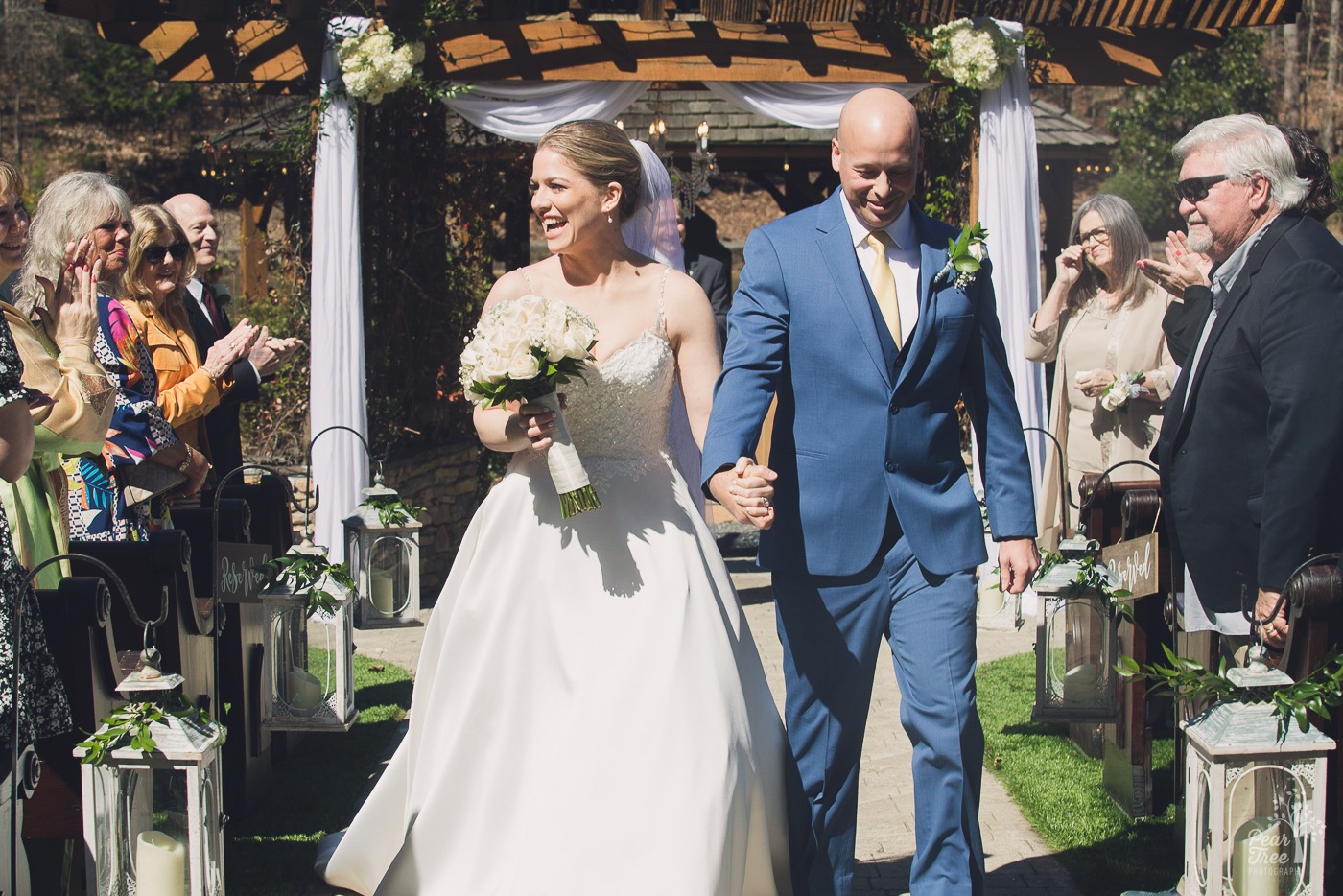 Bride laughing and holding her groom's hand as they walk back down the aisle together