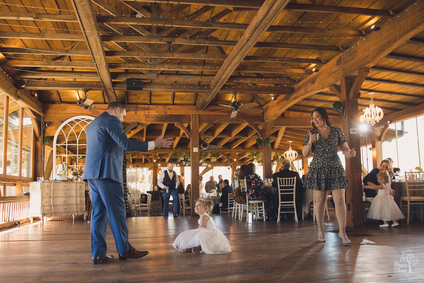 Cute flower girl sitting in middle of dance floor as others walk by