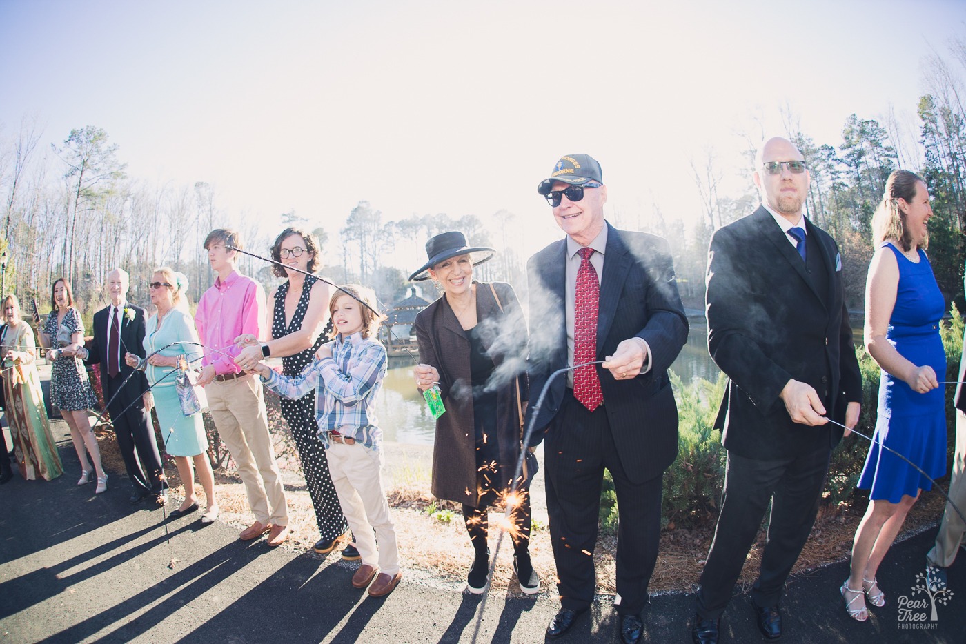 Wedding guests smiling and holding lit sparklers during a daytime wedding reception