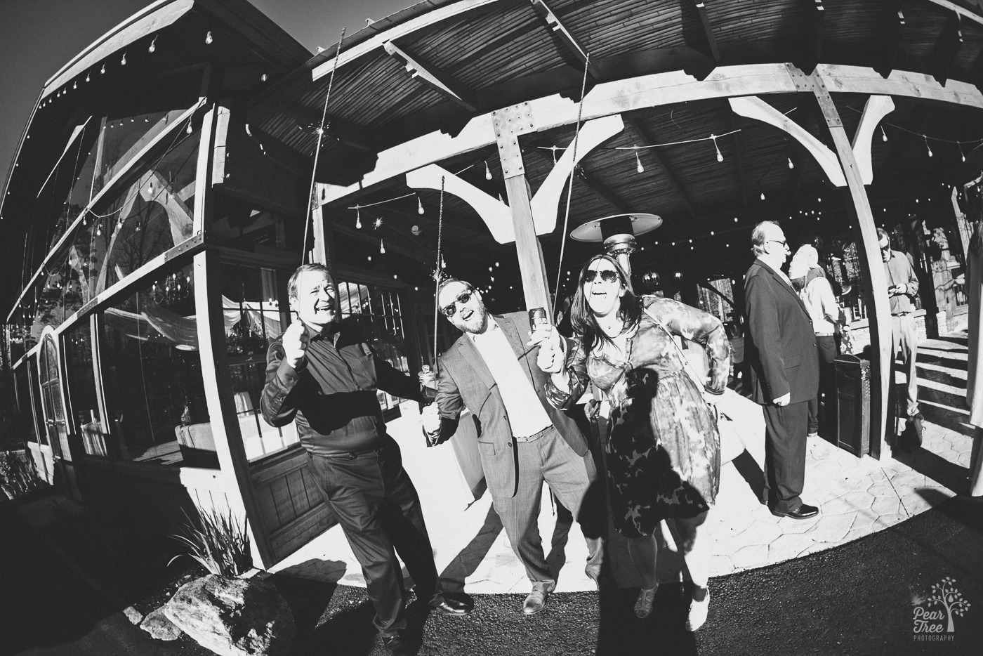 Black and white photo of wedding guests yelling and holding sparklers