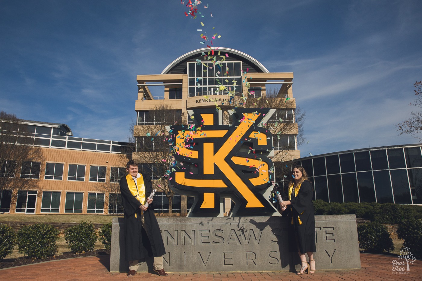 Two excited students launching environmental confetti grenades in front of KSU sign for KSU graduation photos