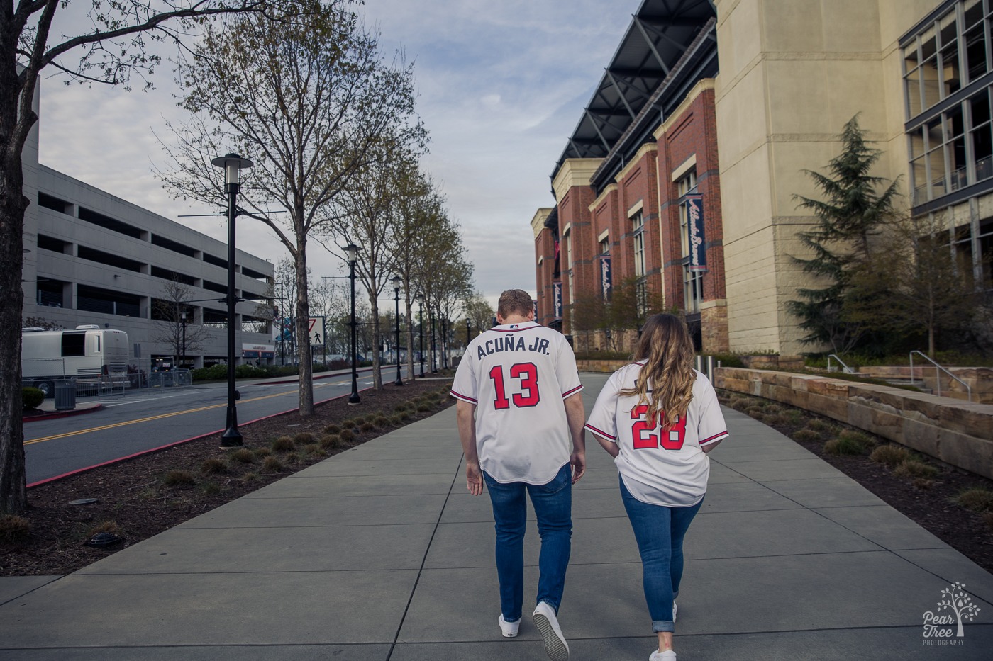 A man and woman wearing Braves jerseys walking towards the Atlanta Braves stadium