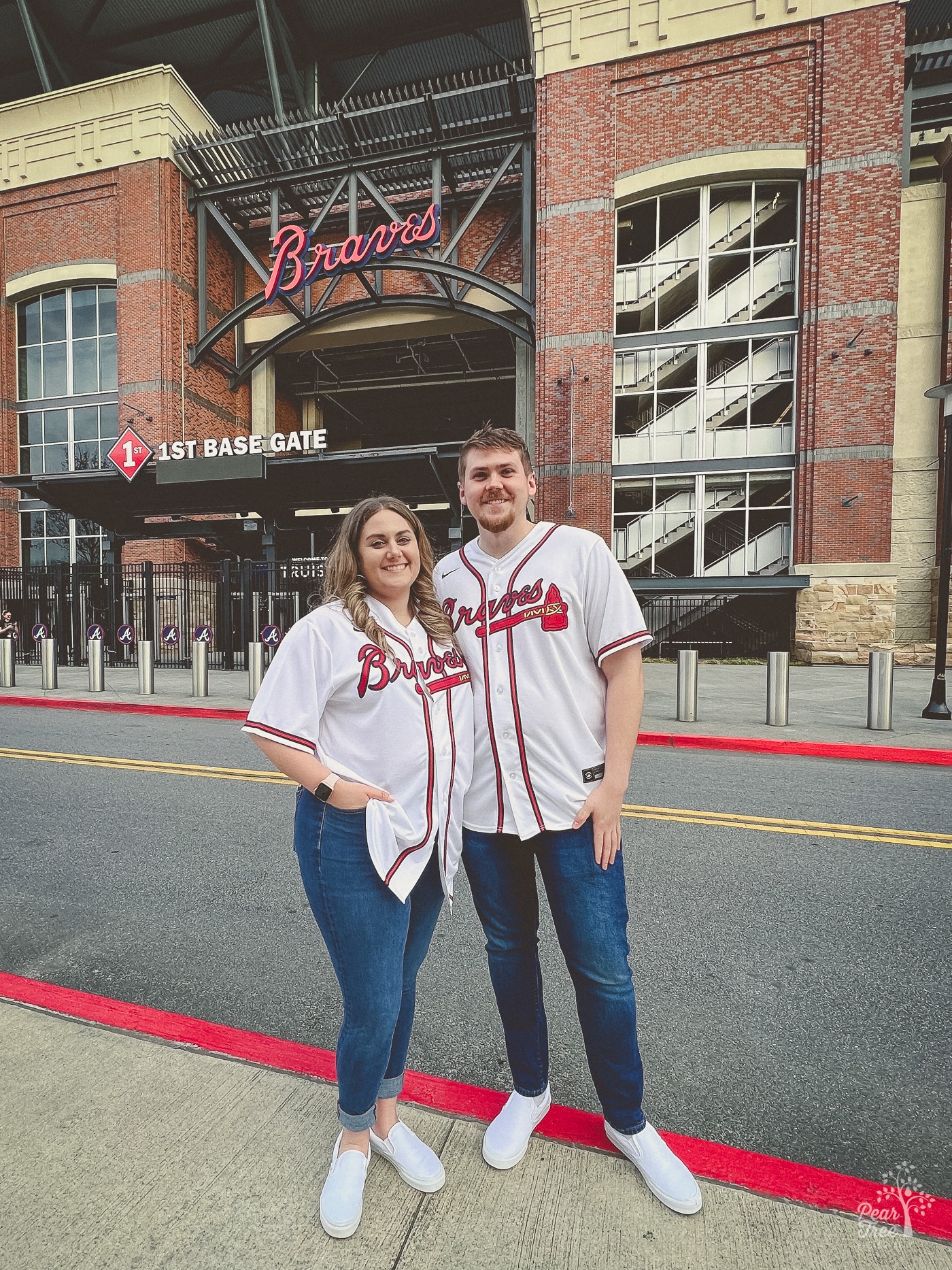 Smiling couple standing in front of the Atlanta Braves 1st base gate wearing sports jerseys