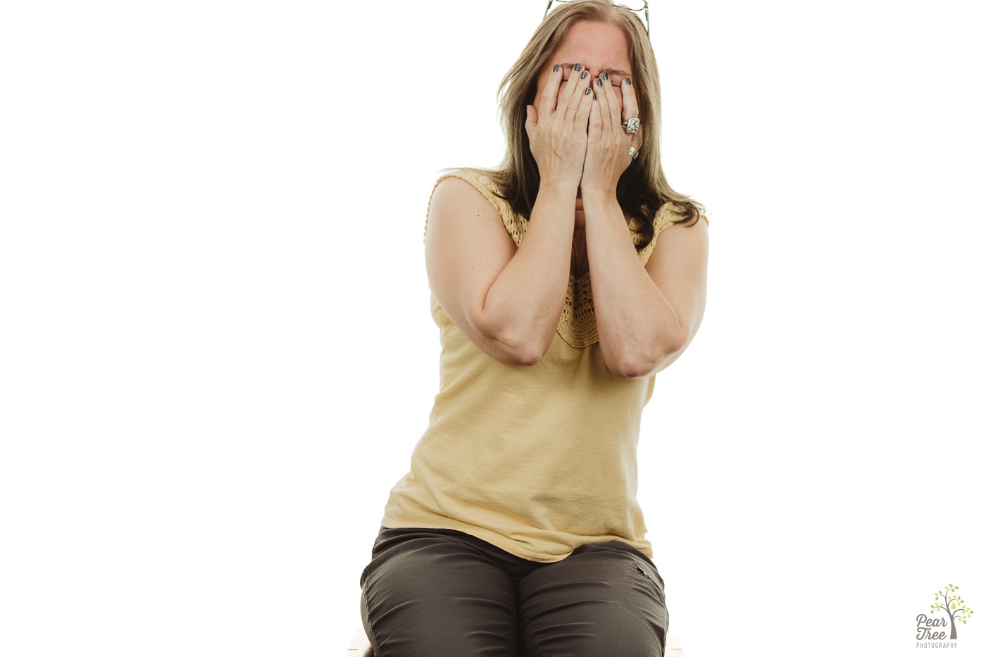 Woman covering her face and rocking to the side while sitting in front of a white background