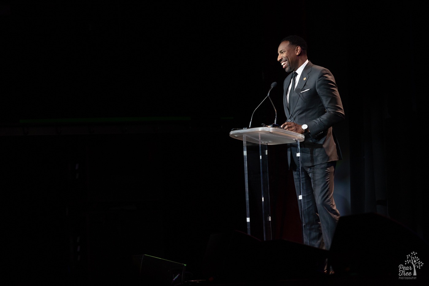 Atlanta Mayor Andre Dickens leaning into a clear podium and laughing on stage at the Coca Cola Roxy