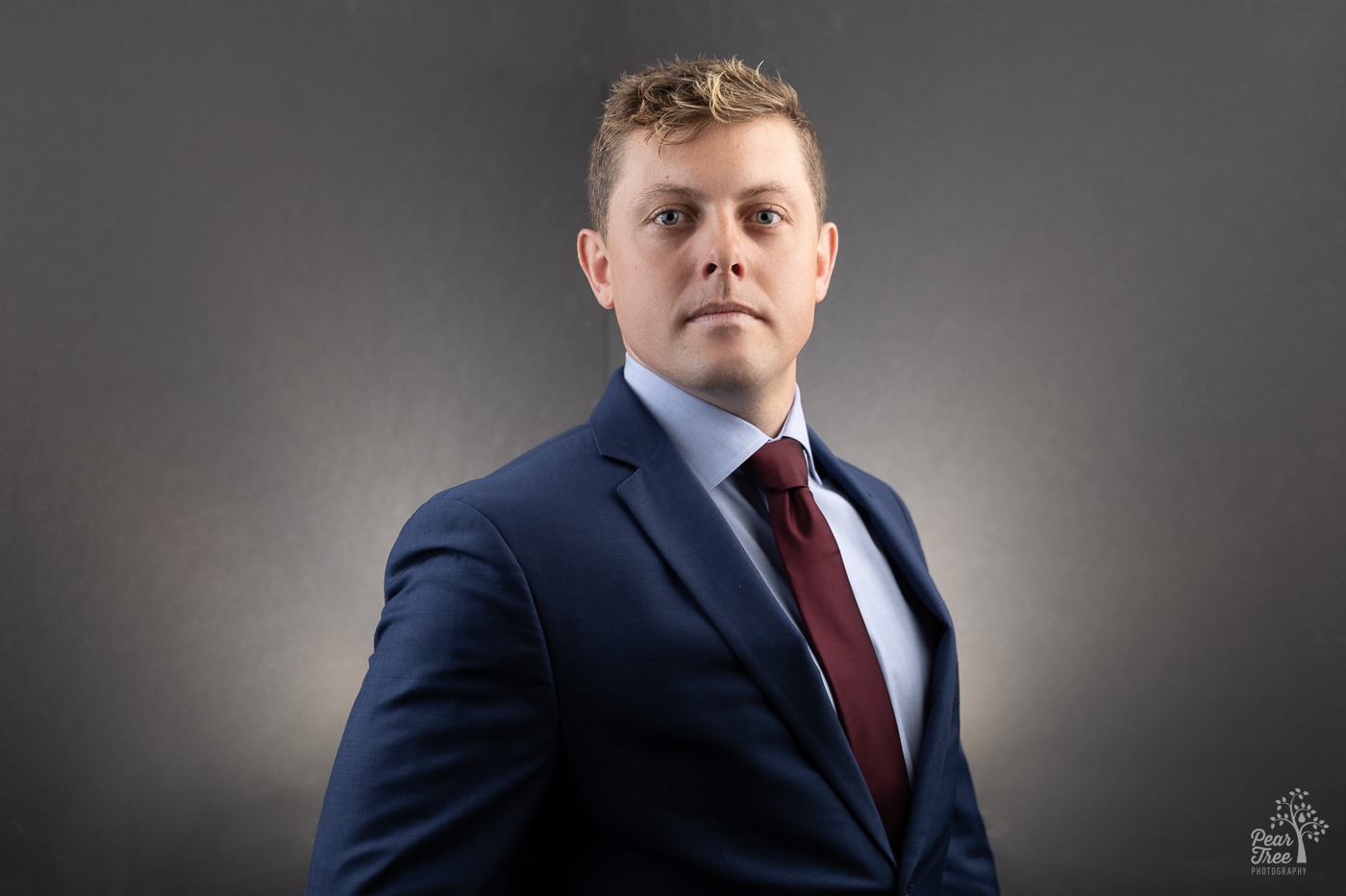 Blond man in blue suit and maroon tie looking very serious for professional headshot photograph in Canton
