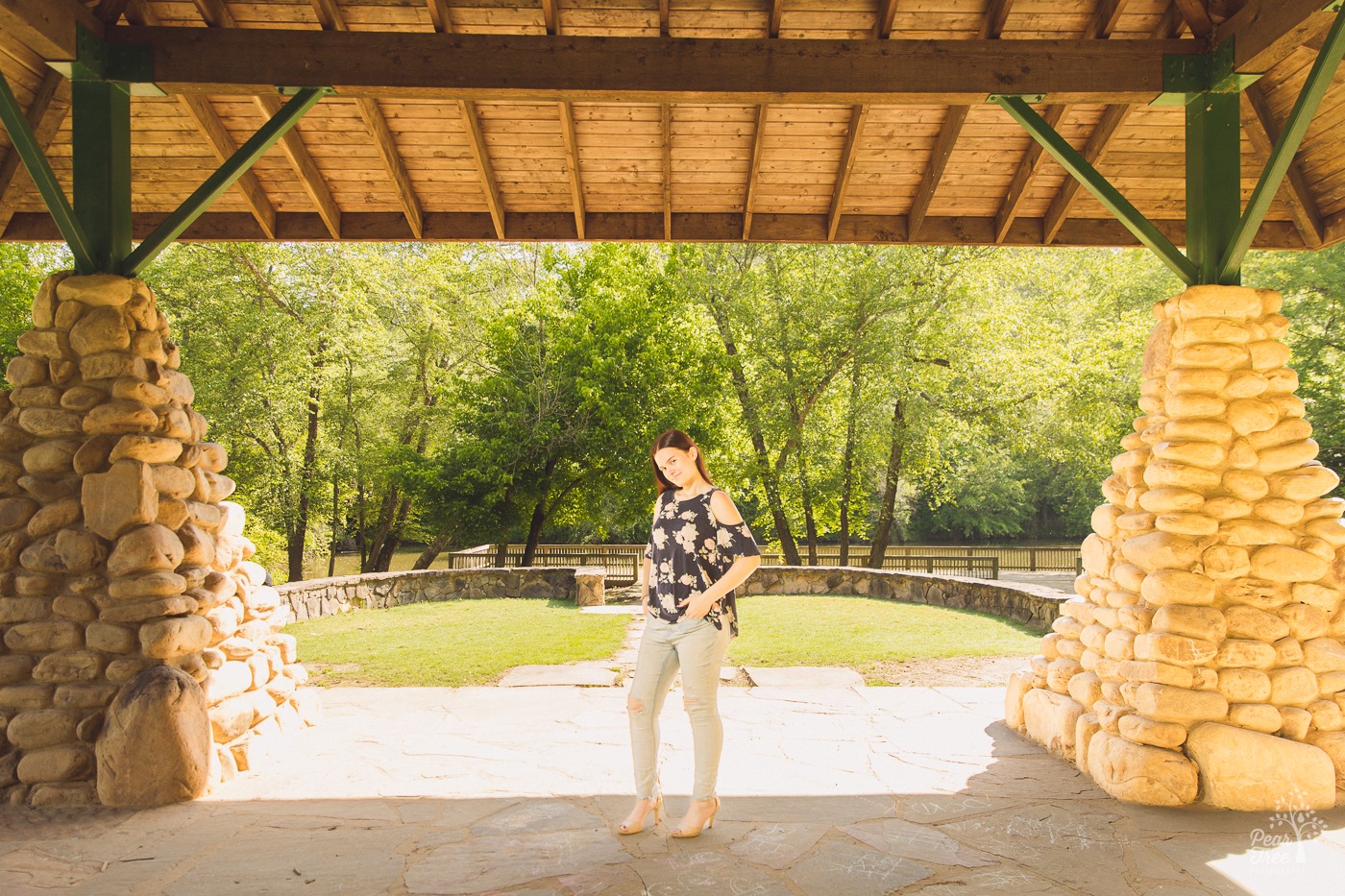 Pretty high school graduate standing in a park with her fingers in jean pockets