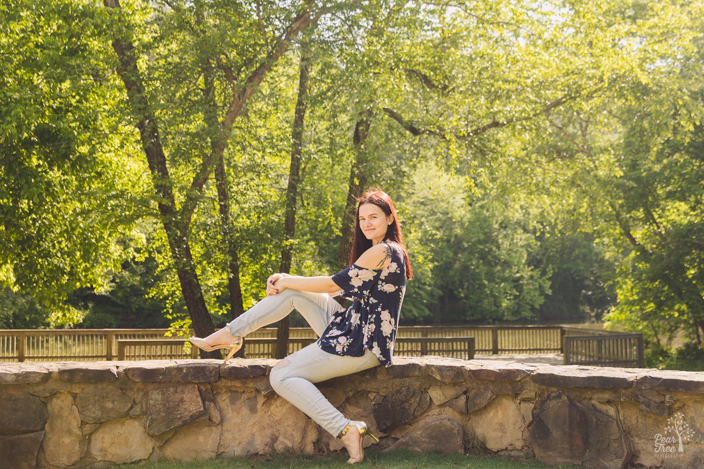 Cute high school senior posing at Olde Rope Mill Park wearing ripped jeans, high heels, and a cute top with Little River in the background