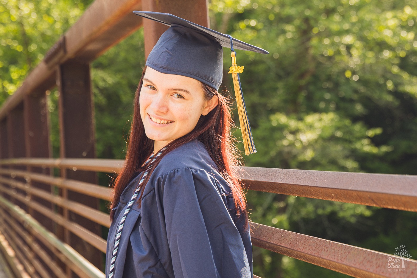 Smiling River Ridge High School senior in cap and gown on a bridge