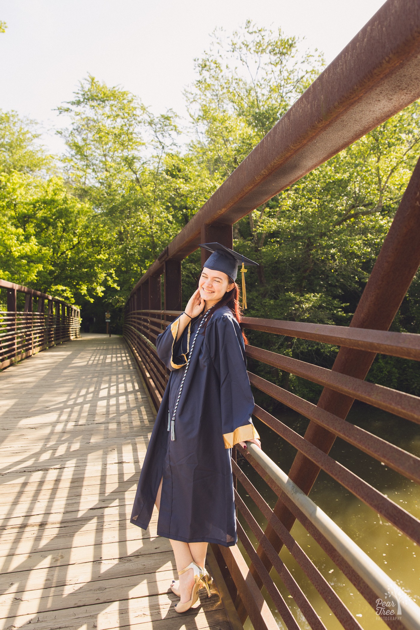 Pretty River Ridge High School senior in cap and gown standing on Olde Rope Mill bridge