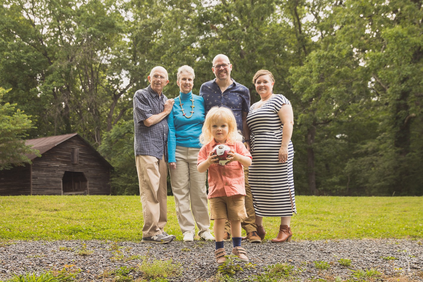 Cute blond toddler boy jumping in front of his parents and grandparents for multi-generational family photos