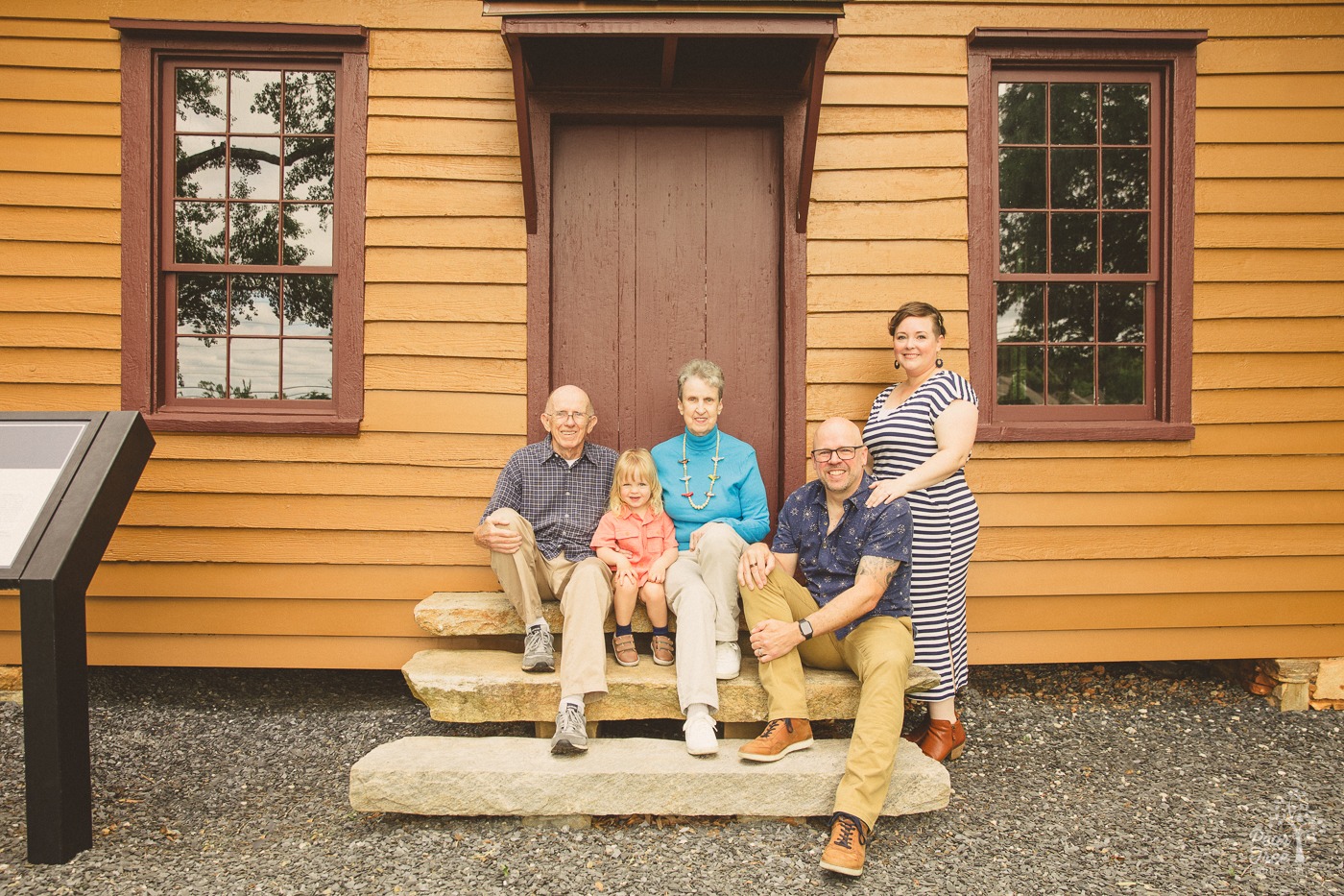 Multi-generational family photo with toddler, his parents, and the grandparents smiling on front stone steps