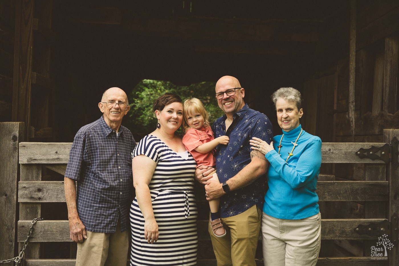 Multi-generational family photo of a toddler with his parents + grandparents in front of a barn