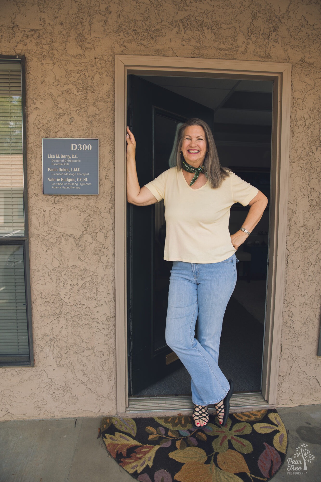 Valerie Hudgins standing in her Roswell office doorway smiling next to her suite sign during her branding photography session